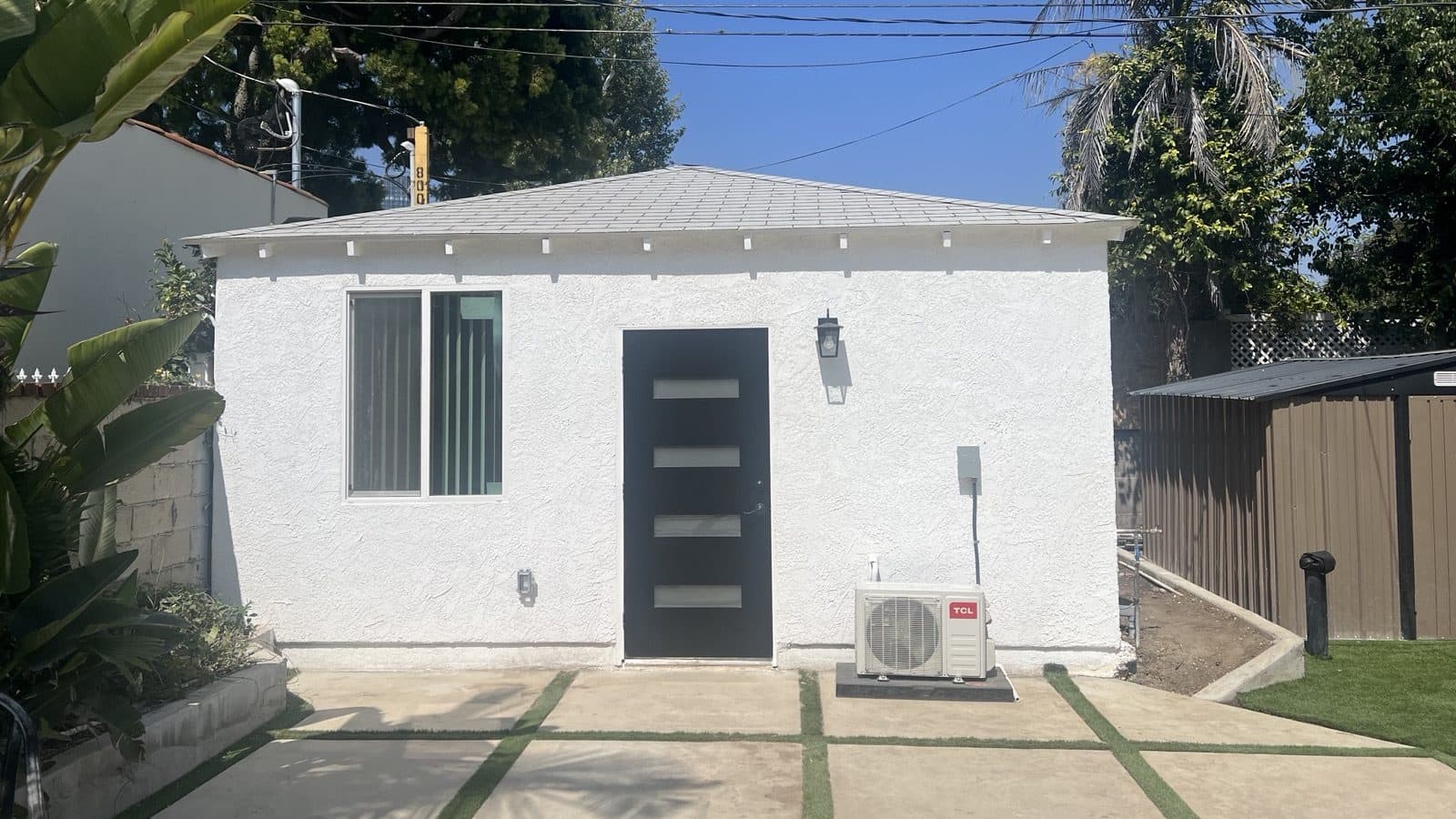 Finished white stucco ADU with a modern black entry door and paver walkway