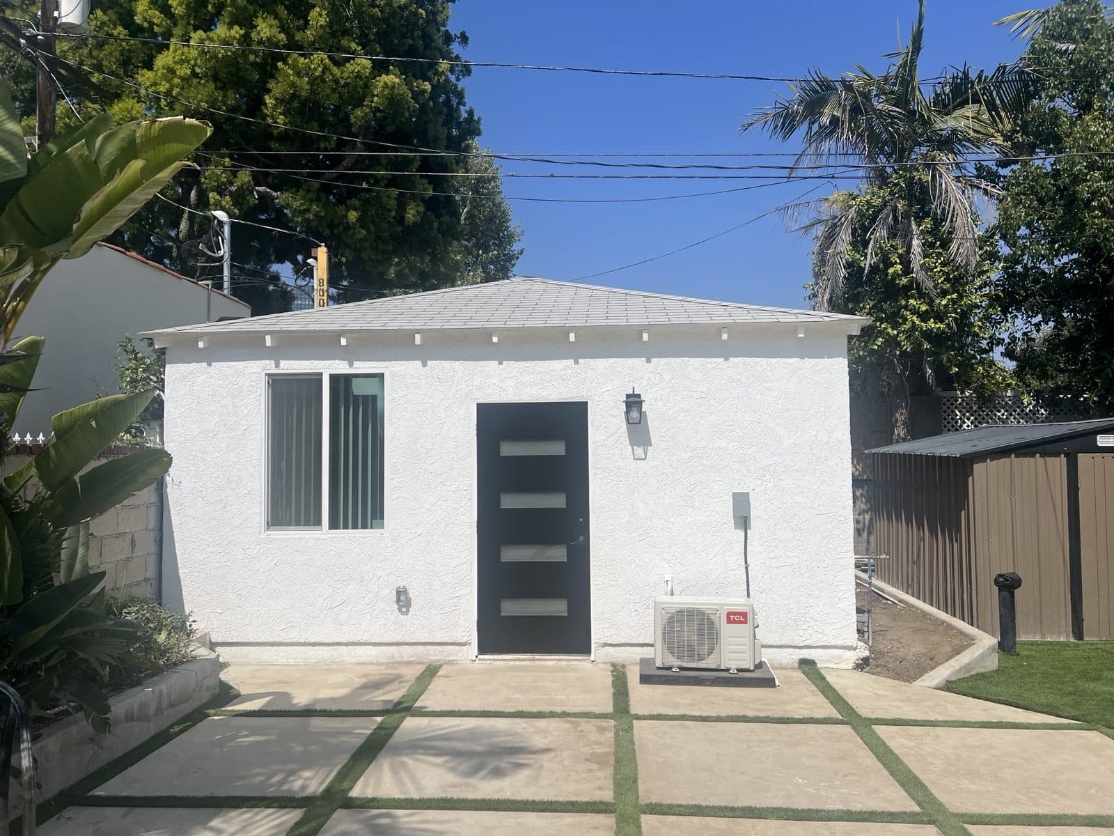 The same structure finished as an ADU with smooth white stucco, a modern entry door, and a paver walkway
